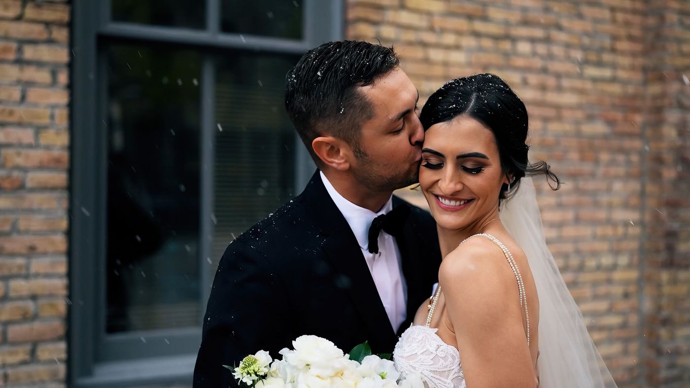 Groom kissing bride on the cheek in falling rain
